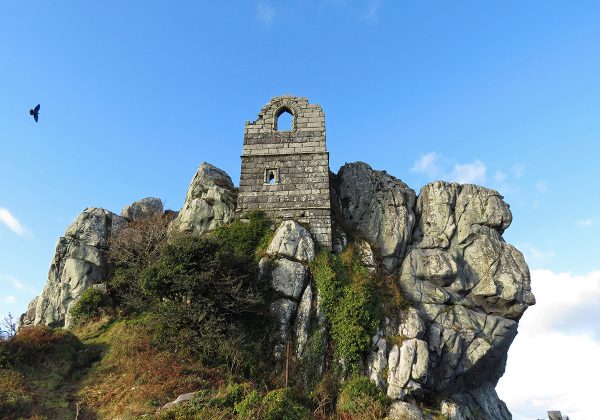 ruined stone tower on clifftop, single bird in blue sky