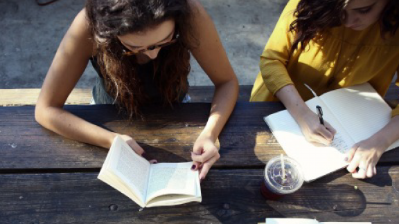 Two young women reading and writing at an outside wooden table