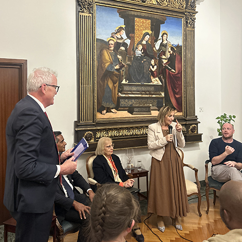 Cristina Gangema talking into a microphone, three people on a panel watching.