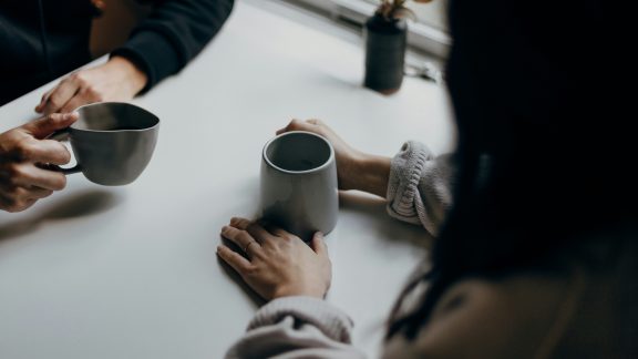 Two people holding cups of tea, only hands and arms showing