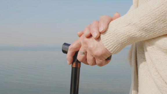 older person's hands leaning on walking stick