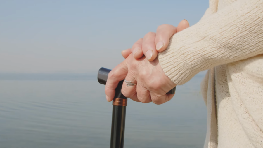 older person's hands leaning on walking stick