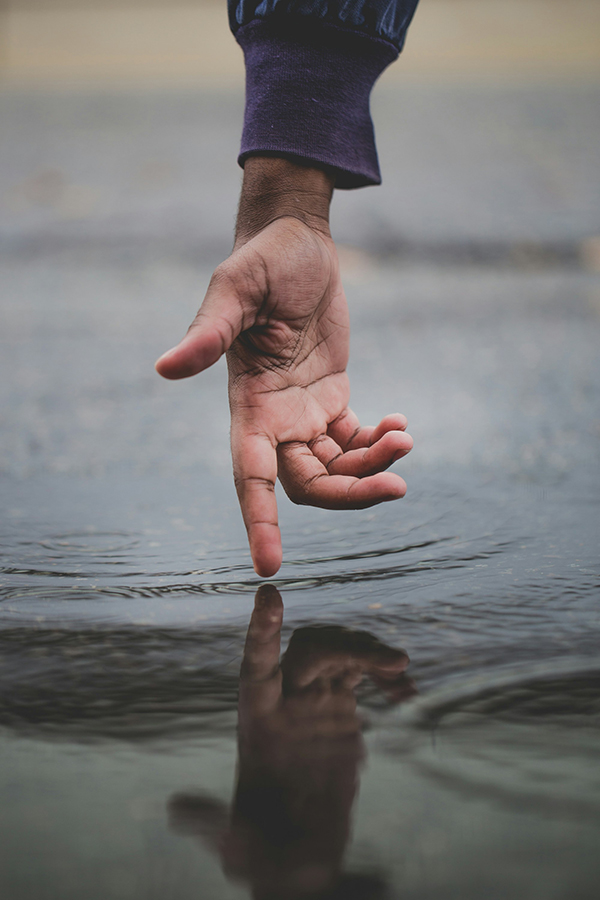 Hand above water reaching down, finger touching surface