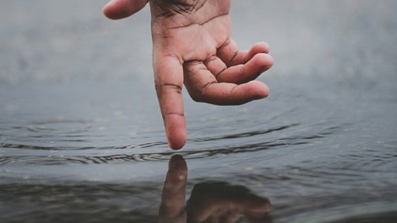 Hand above water reaching down, finger touching surface