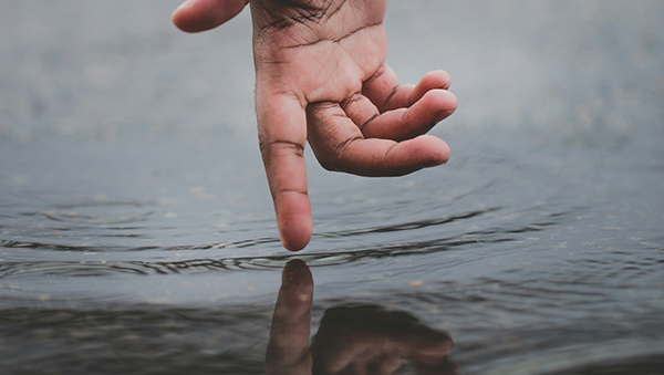 Hand above water reaching down, finger touching surface