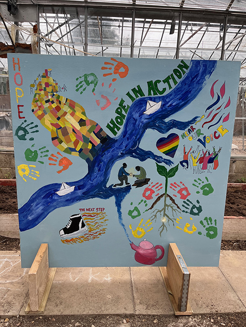 Painted colourful mural with a river, handprints and the words 'hope in action'